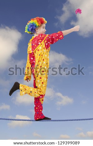 clown as a tightrope walker with flower, blue sky with clouds