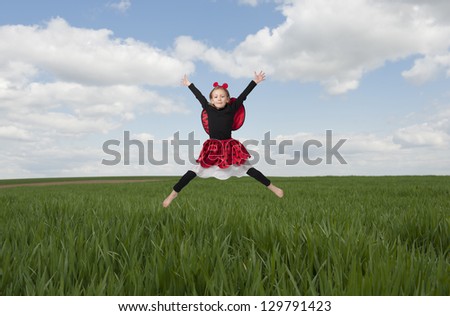 little girl in lady bug costume jumping in the fields, arms wide open