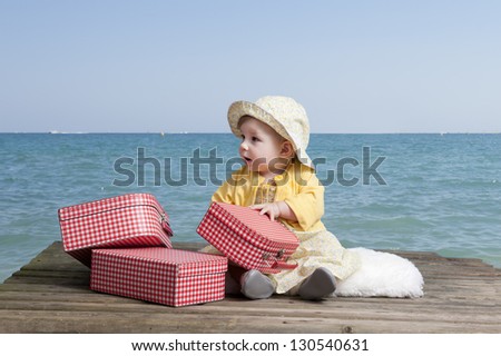 little baby girl with vintage suitcases on an old wooden raft floating in the sea