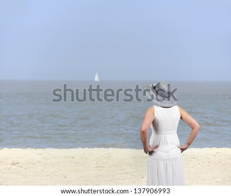 back view of a young woman in white dress with hat at the beach
