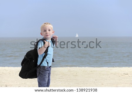 little boy with heavy backpack , outdoors at the beach