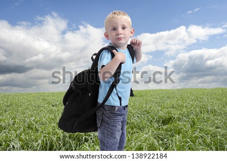 little boy with heavy backpack, outdoors in meadow