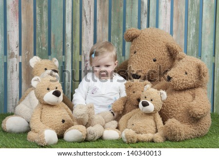 baby girl with group of teddy bears, seated in front of a fence