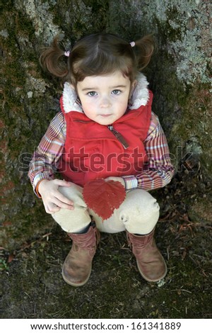 little girl with pony tails seated against a tree looking up