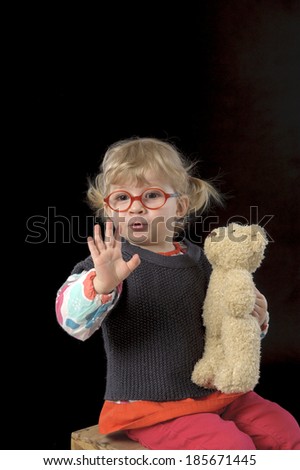 little toddler with glasses and teddy bear saying hello on black