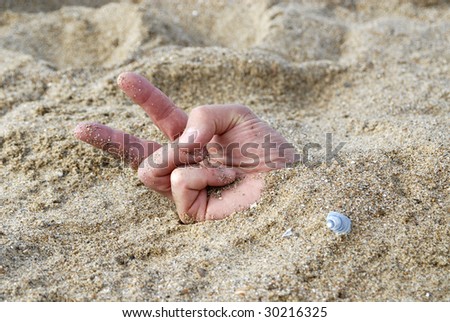 hand buries in the sand making a victory sign