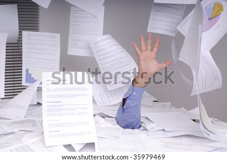 Hand of business man sticking out of a desk full of papers and flying papers