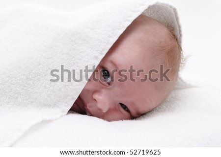 small baby peeping from under a white sponge towel
