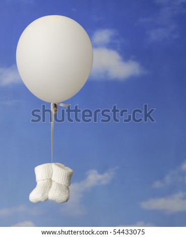 birth concept: white baby booties hanging onto a white balloon against a blue sky with clouds