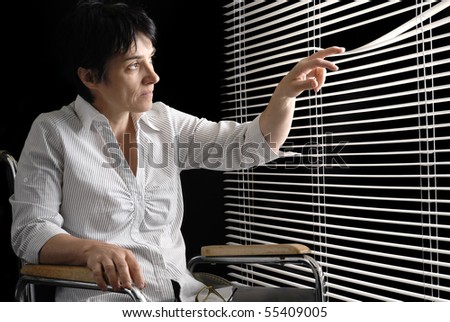 Disabled woman in wheelchair looking trough blinds