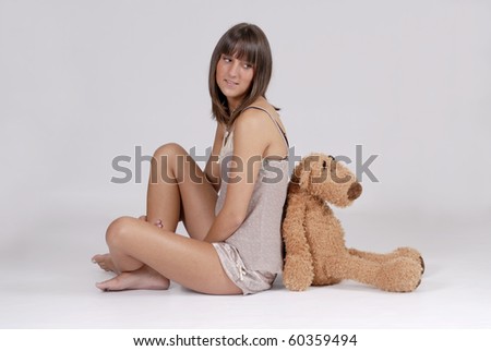 beautiful young blond woman in  nightie sitting back to back with a teddy bear