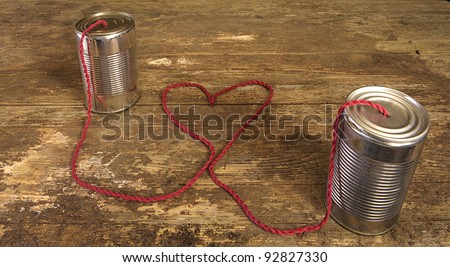 tin can phone with heart shape in wire on old wooden surface