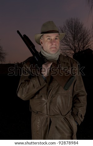 man with cowboy hat, long leather coat and riot gun at night