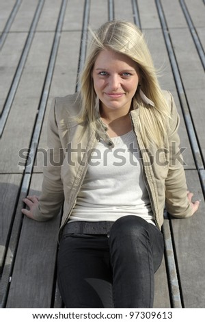 Beautiful younG blond woman seated on a wooden floor outdoors in the sun