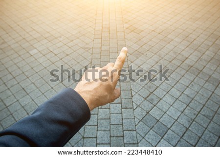 Male hand pointing the finger forward to the light on grey brick background