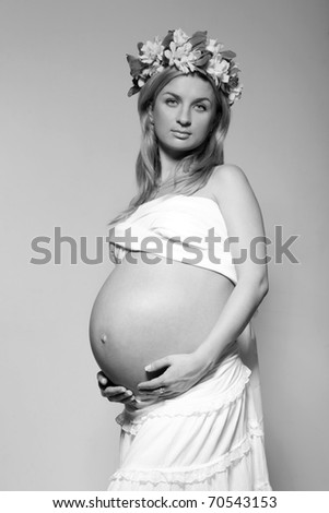 black white pregnant blond young woman holding her belly with bouquet of flowers on her head