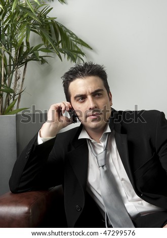 Business man chatting on his cellphone, sitting on sofa looking stressed.