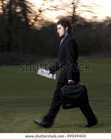 Business man walking briskly, carrying a brief/laptop case and a newspaper.