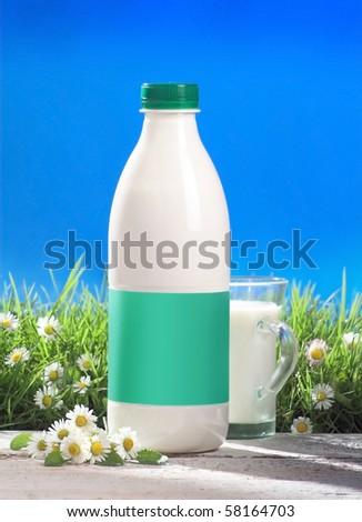 bottle and glass of milk with blank label outside, grass and flovers