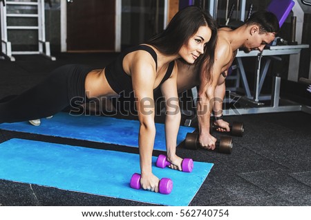 A guy and a girl in a gym doing fitness , sport . the guy winds elastic bandages on the fingers . girl drinks water and splashes it on his chest . tattoo