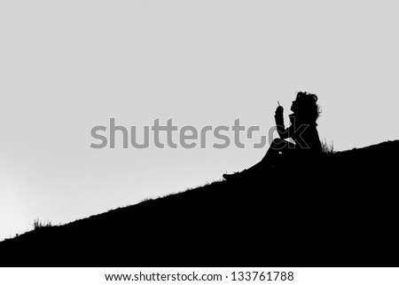 A Silhouette of a girl seated on the ground, smoking