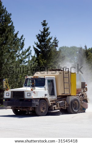 A street sweeper truck with a dust cloud behind.