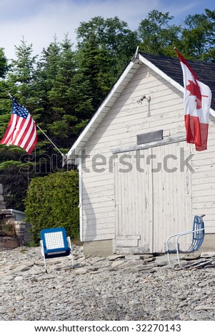 An old boathouse with American and Canadian flags on either side, with two chairs in front.  On the shores of Georgian Bay, in the Bruce Peninsula.