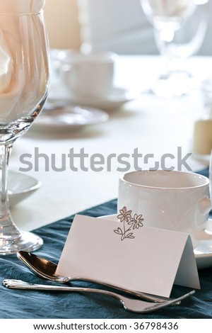 A closeup of a blank wedding placecard in front of a coffee cup, and other items on the table.