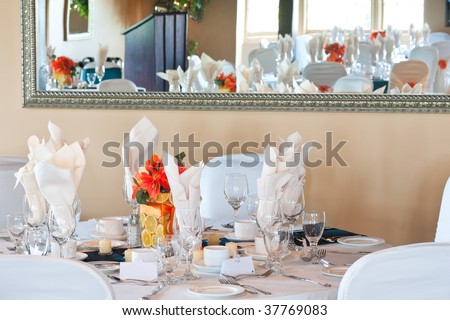 A full table wedding place setting, complete with an orange center piece, with a mirror behind, reflecting the venue including a podium.