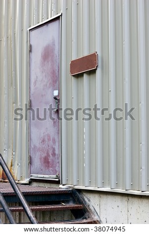 The back door of a retail store, with a blank sign beside, and stairs leading up to it.