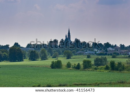 A picturesque landscape of farmland in Southern Ontario, with a small town church on the hill in the distance.