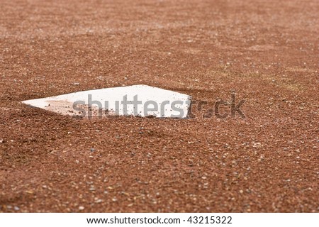 A closeup of home plate with surrounding reddish brown gravel at a baseball diamond.