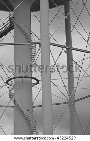 The supporting columns beneath a water tower, including the winding staircase that leads to the top.  A black and white treatment has been applied to the image, giving the overcast sky more mood.