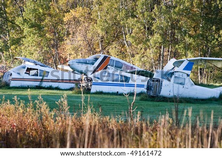 A plan graveyard in the country, showing many pieces of old prop planes in a field.