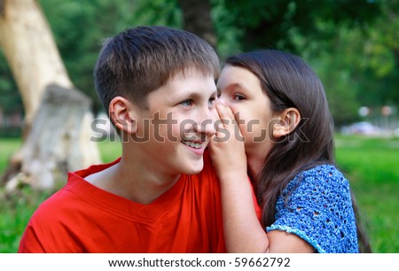 the girl whispers to the boy a secret outdoors