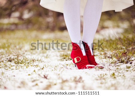 feet of the girl in red shoes and white stockings stand on snow