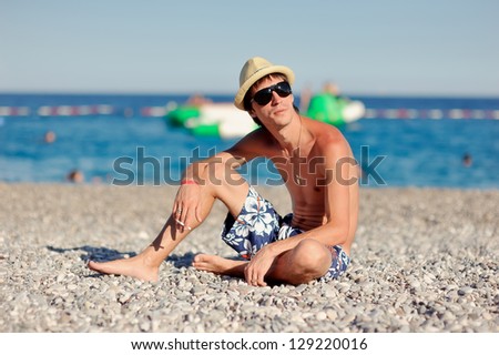 young man in sunglasses and a straw hat sitting on the beach