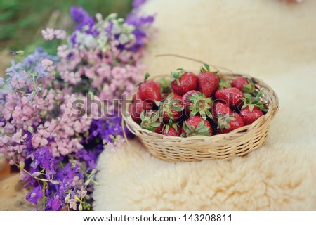 beautiful composition with a fur in a wicker basket strawberries and a bouquet of flowers