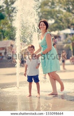 mother in a turquoise dress with a young son playing at the fountain