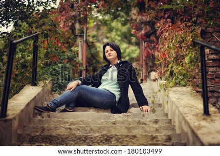 in the park on the stairs with black railing woman sitting in a black coat and trousers