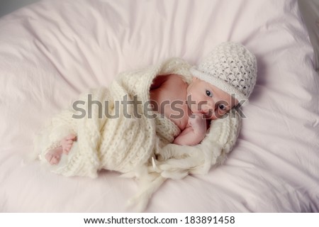 little baby wrapped in a knitted blanket and a white knitted cap