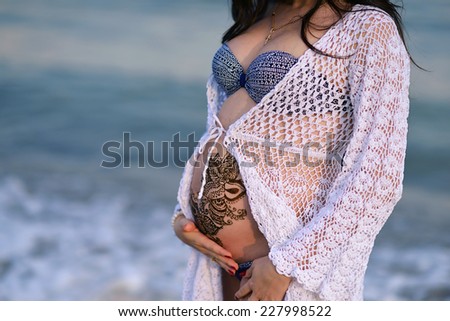 on sea background pregnant woman\'s belly with a beautiful girl in a white lace blouse