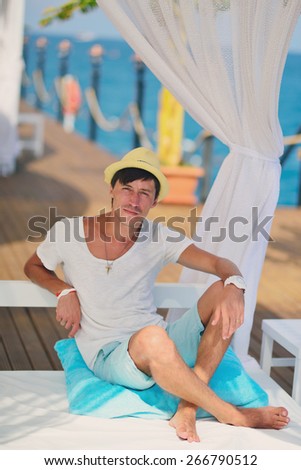 against the sea under a white canopy resting man in a straw hat