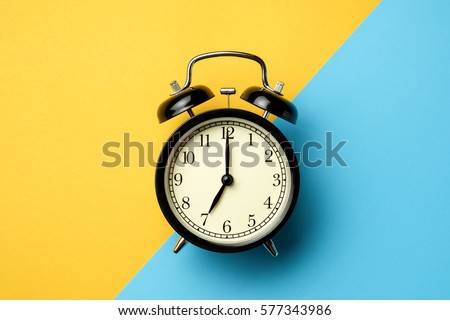 black vintage alarm clock on two tone color yellow and light blue background
