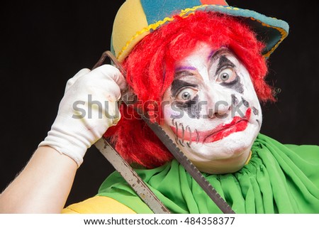 Scary creepy clown joker with a smile and red hair with a saw on a black background