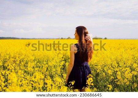 Rear view of young woman with hand in long hair on yellow blooming rapeseed field