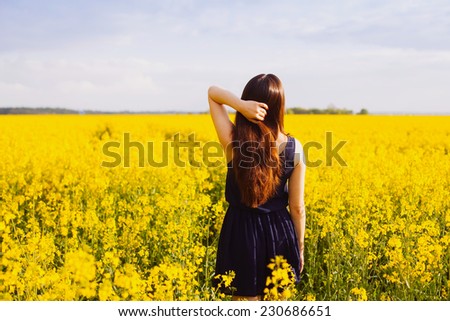 Rear view of young woman with hand in long hair on yellow blooming rapeseed field