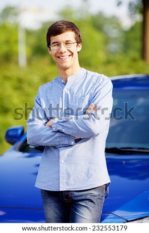 Handsome smiling guy wearing glasses standing in front of car with crossed arms