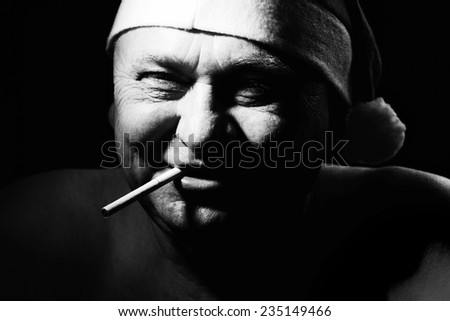 Close up black and white portrait of smiling mature man in Santa Claus hat and with cigarette in his mouth