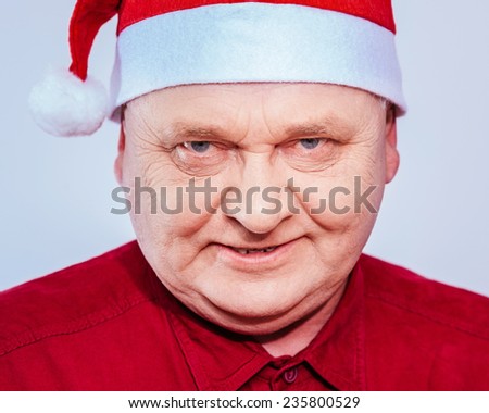 Close up portrait of evil aged man in Santa Claus hat and red shirt over white background